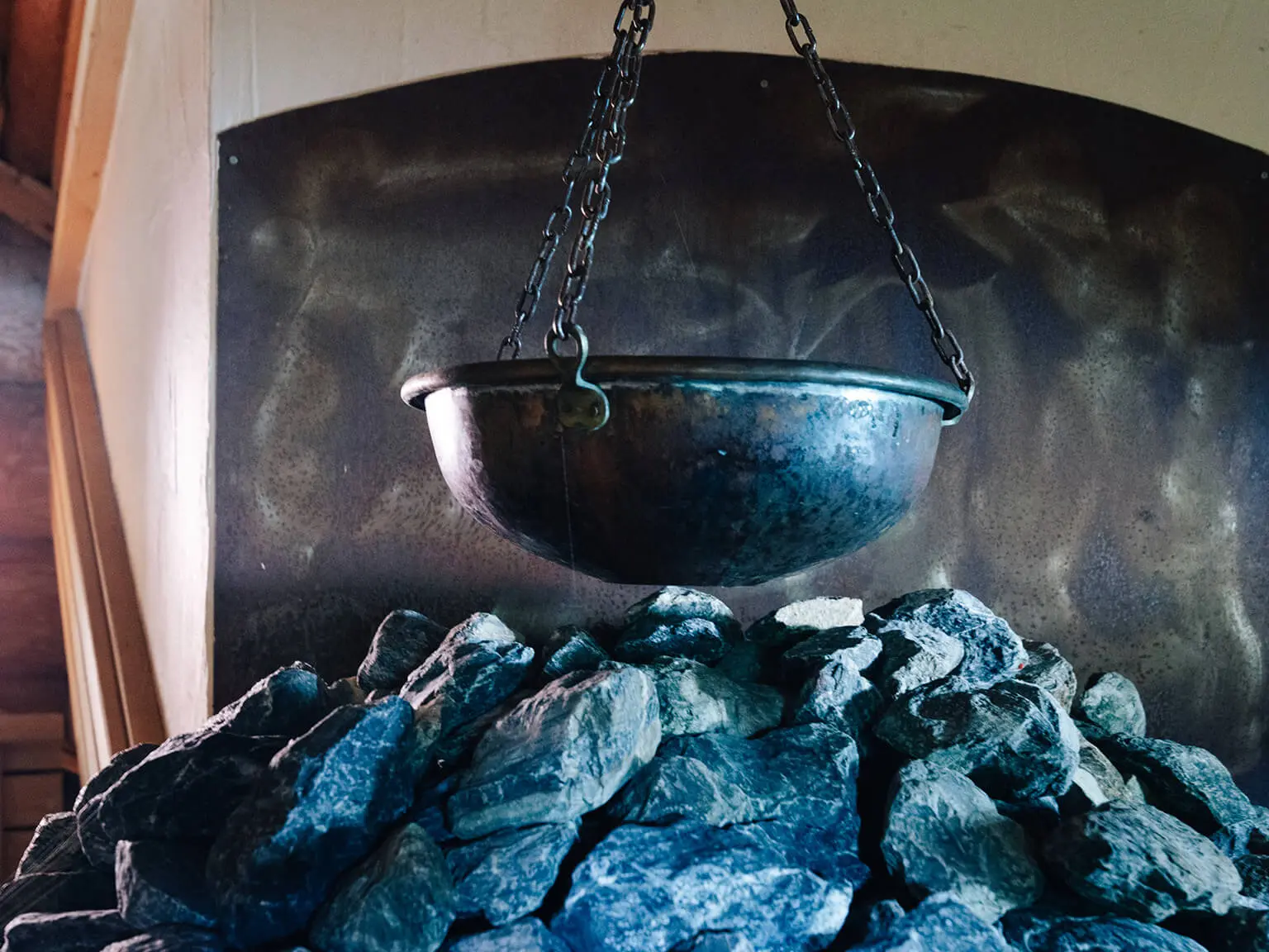Eine Metallschale hängt an Metallketten über einem Haufen Steine in einer Sauna