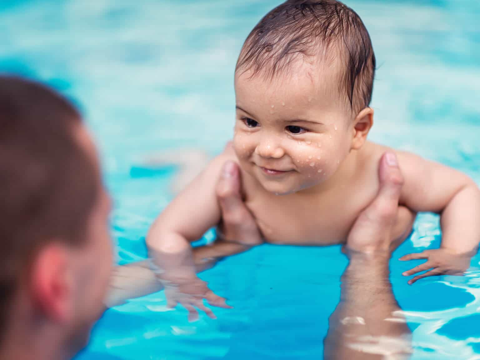 Ein Baby wird von seinem Vater beim Babyschwimmen im Wasser gehalten
