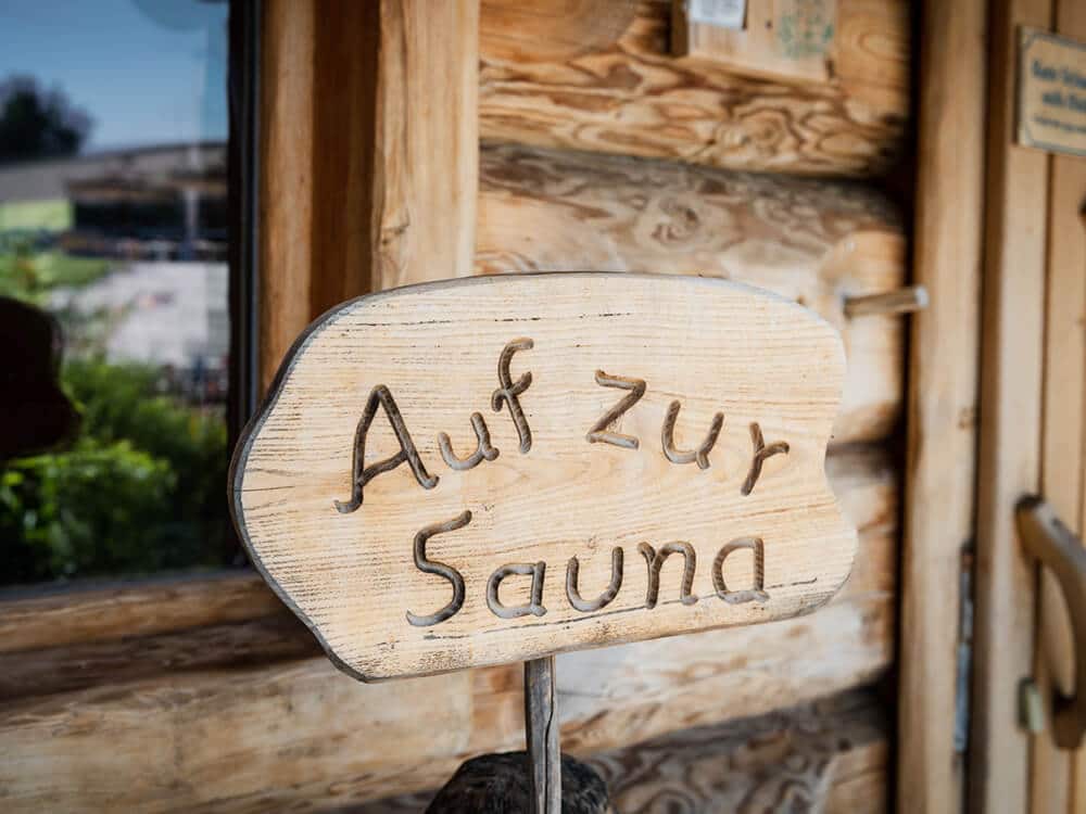 Auf einem Holzschild vor einem Blockhaus steht "Auf zur Sauna"